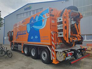 Saugwagen - Apken GmbH Ein großer orangefarbener Saugwagen ist vor einem Gebäude abgestellt.