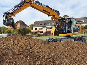 Bagger - Apken GmbH Ein großer Erdhaufen wird durch einen Bagger auf der Baustelle bewegt.