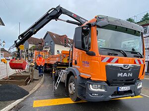 Pritschenwagen / Kastenwagen Ein großer orangefarbener Kranwagen steht auf der Baustelle und wird durch einen Mitarbeiter bedient.