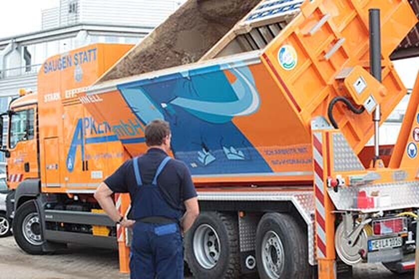 Saugwagen - Apken GmbH Ein großer orangefarbener Saugwagen von der Seite beim entleeren.